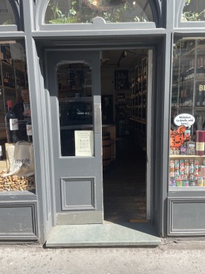 View of the main entrance to the venue, located at the middle of the shop front. There are double doors which push open from the middle. There is a step at the foot of the door.