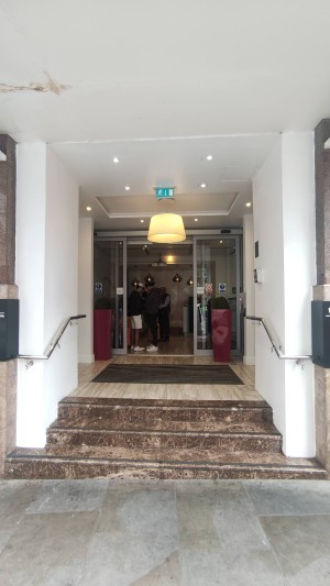 Brown staircase ahead. Silver handrails on both sides of wall. Automatic door to hotel straight ahead.