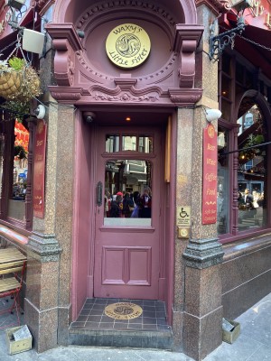 Directly facing door entrance into venue from outside with one step along front. Door handle on left side of door. Door bell for assistance on right side of door.