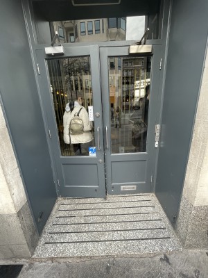 Double glass door, with grey wooden doorframe. Silver handles at centre. Pull to open. Built-in ramp before door.