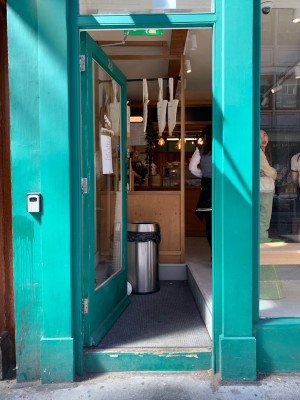 Single glass door with green wooden frame. Push from gold metal handle on right of door to open.