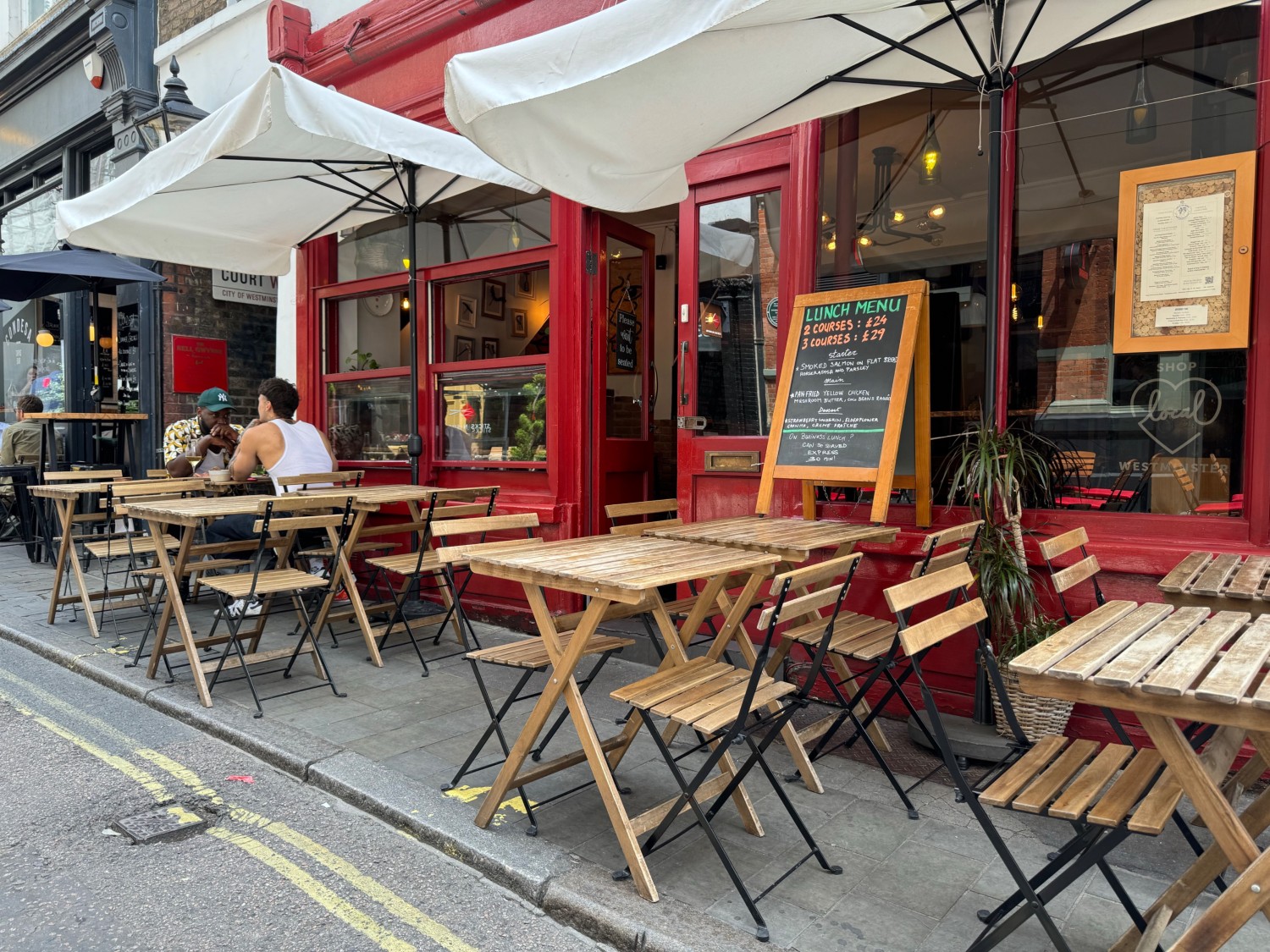 Outdoor seating area on street with seated height tables and chairs and adjustable shelter. One step to access seating area from street