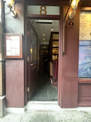 Preceding single brown wooden door with large glass panel. Vertical gold metal handle right. Push to open.
