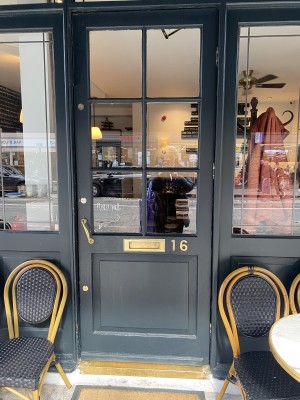 Directly facing the door entrance into the venue from the path. Chairs on both sides of door & door in middle. Door handle on left side at seated height and you pull door outwards.