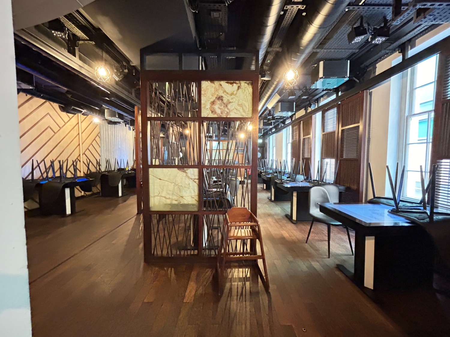 From top of stairs, facing straight. Tables and chairs along left, right and middle. Wooden divider ahead. Paths on left and right.