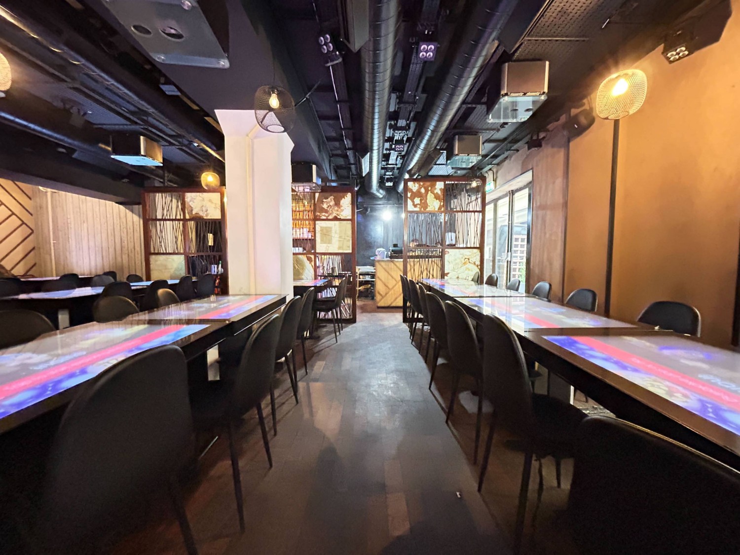 From start of seating, looking left. Tables and chairs along left and right. Path in middle. Wooden partition at back.