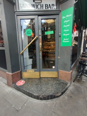 Access via double glass door with grey frame. Push open via metal handles in center.