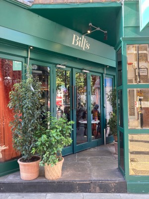 From street, facing venue. Path to main entrance proceeds ahead between plants on left and reflective pillar on right. Entrance at end of path to left