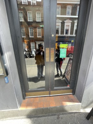 There is large step before the double doors. The double doors are push doors, pushed in the centre where the doors meet. There is an assistance button to the left of the doors.