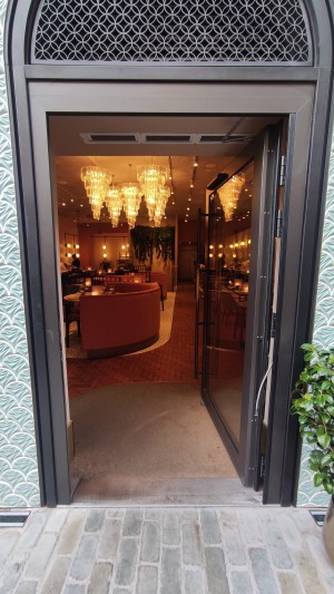 Glass door with black frames ahead. Push to left via vertical brass handle to open.