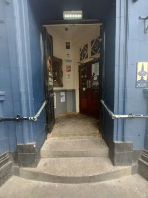 Picture of main entrance. There are two sets of double doors. The first door has handrails on both sides. There are three steps to the first door. The door is held open, you have to push it open from the middle.