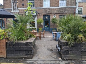 From pavement facing venue. Planters on left and right. Outdoor seating behind.