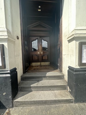 Wooden doors with metal handles in centre. Push to open. Steps before doors. Doorbell left of doors.