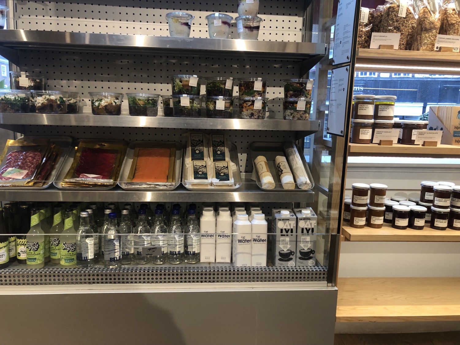 Food and drinks displayed in open-front fridge and on shelves in self-serve area. About half is accessible from average seated height but half needs average height range person standing to reach.