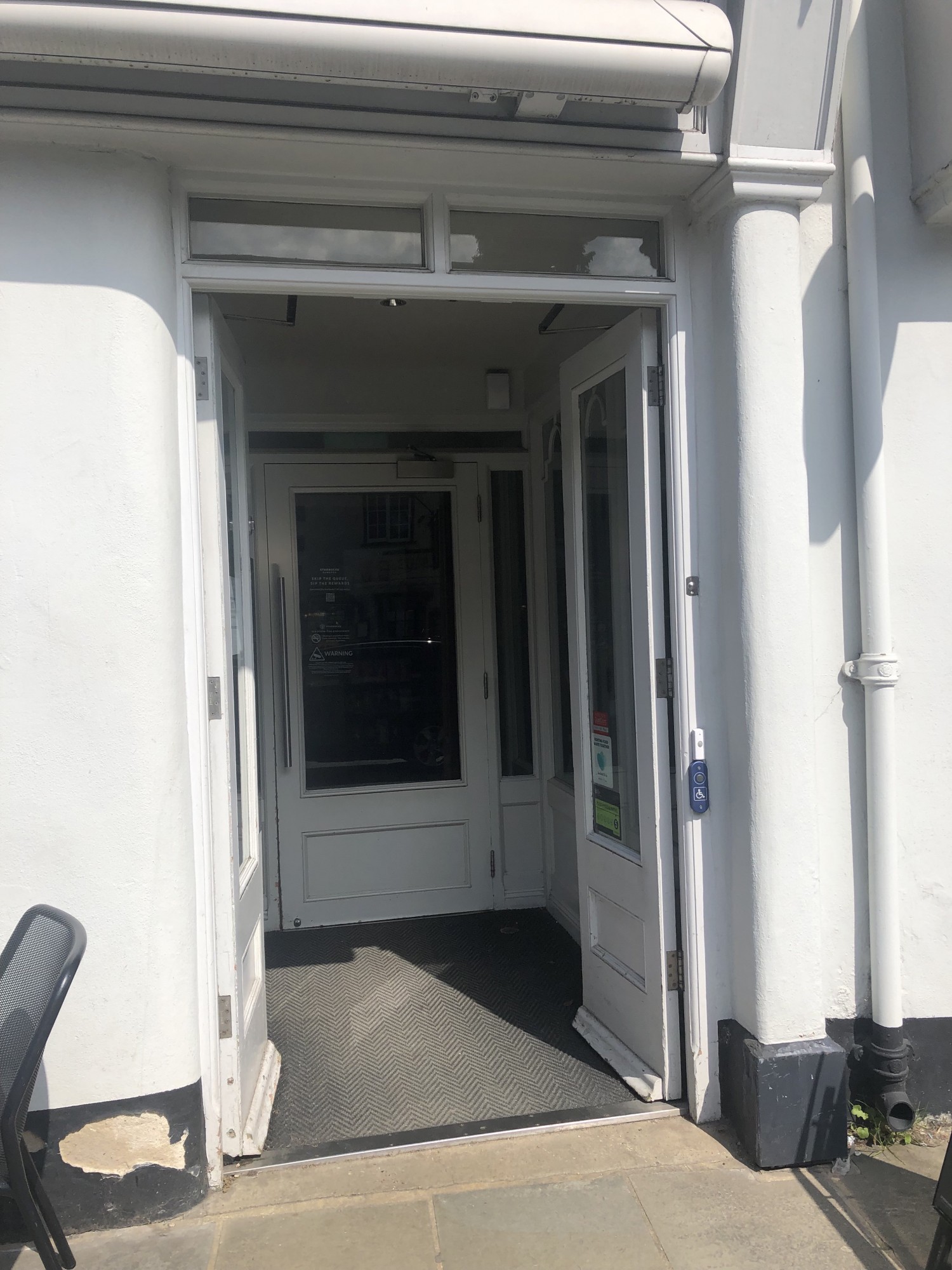 Entrance with outer and inner doors, both white painted wood with glass panes in. Inner door has long horizontal bar. Both are heavy.