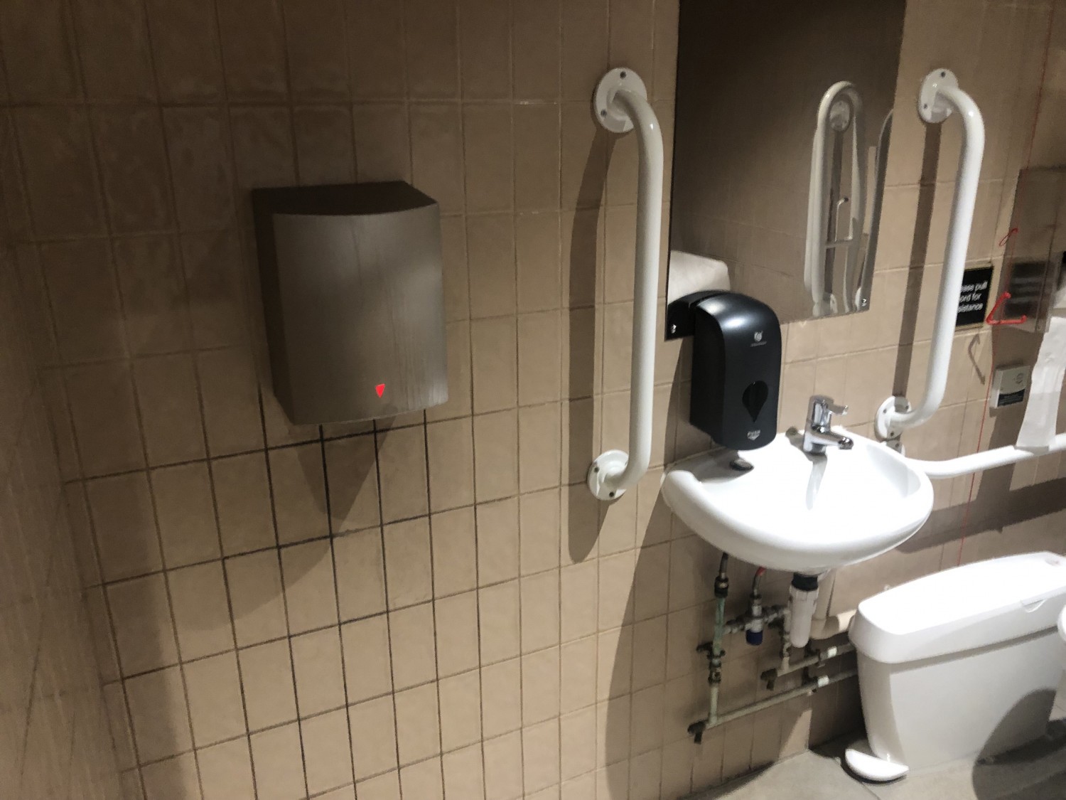 Hand dryer on wall on left. Then sunk, grab rails and sanitary bin on right.