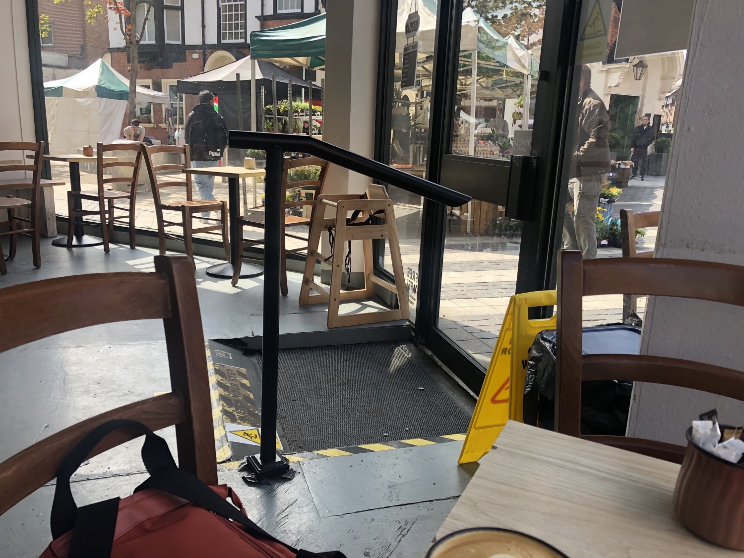 Interior view of main door with step turned into small steep ramp, trip hazard warning tape and stickers. There is a black handrail on the left of the door as you enter