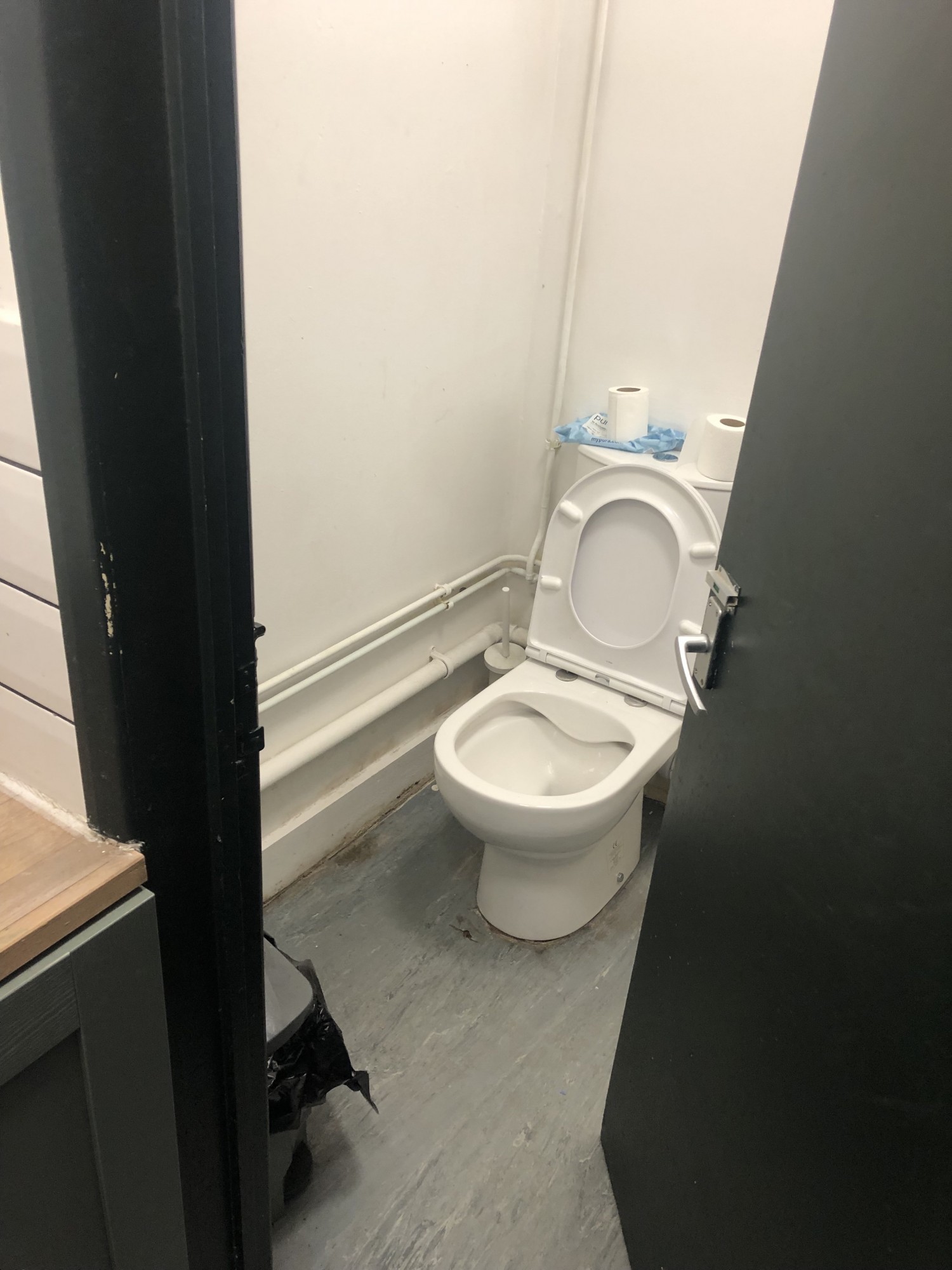 Dark narrow doorframe and door open to show small bathroom with white bathroom