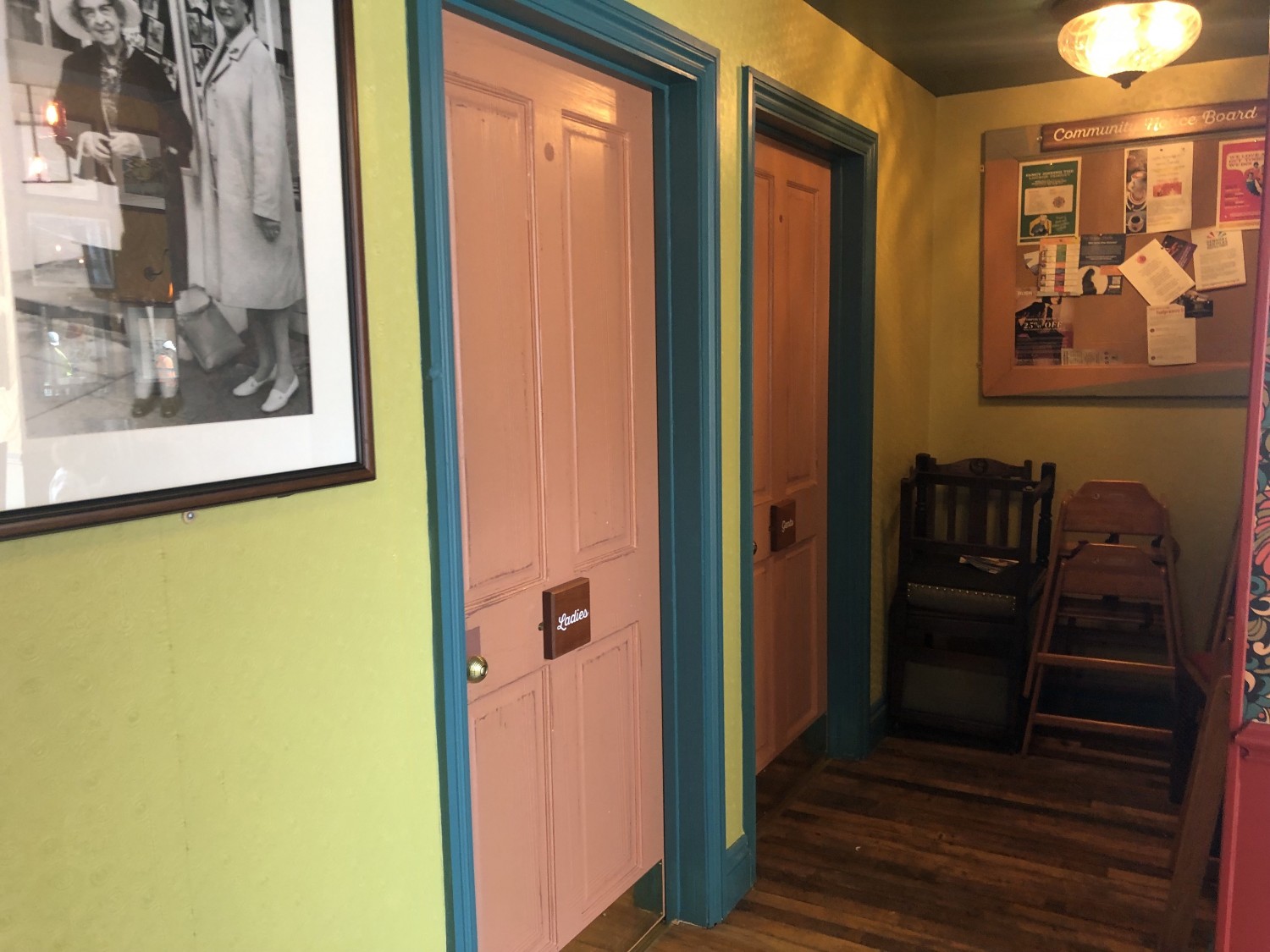 Colourful entrance to men and women’s single sex (not wheelchair accessible) bathrooms. Pink doors, blue frames and green walls. High chairs stacked in corner.