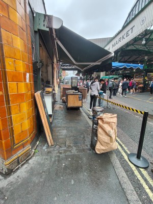 From pavement facing straight. Path ahead to venue on left. Open kitchen tables at back centre. Fence on right.