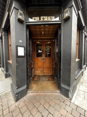 Looking directly at main entrance. Main entrance in corner of venue. First set of double doors are black wood doors with glass in middle. Push in the middle to open.