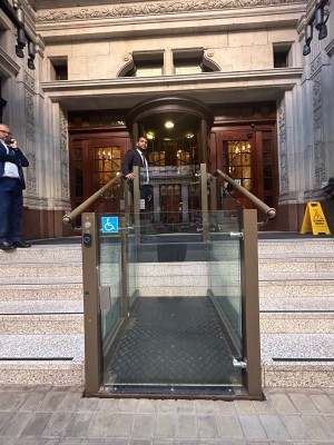 From street facing venue. Platform lift ahead with single glass door. Pull from left to open.