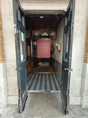 Facing black framed entrance door. Pull silver metal doorknobs at centre to open.