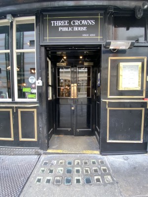 From sidewalk facing venue. Path ahead with a very small step. Black doors after. Pull via gold vertical handles in centre to open.