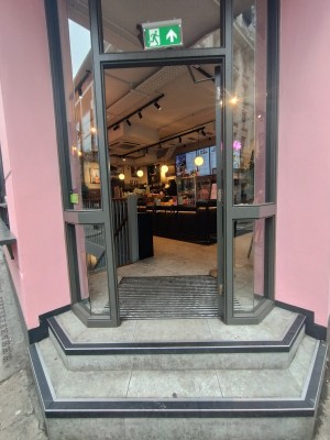 Access via glass door with metal frame. Push open via metal pad on left.
