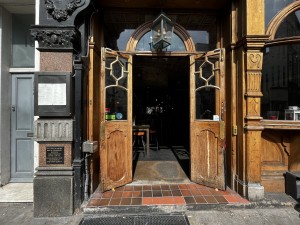 Photo of main entrance door. Two vertical handles in middle of double doors, pull outwards to open. Two steps to access. Call button on right of doorway.