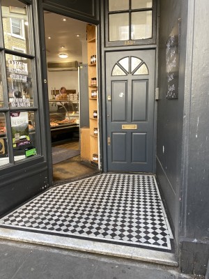 From sidewalk facing venue. Opening ahead to entrance door on back. Black door, push from right to open.