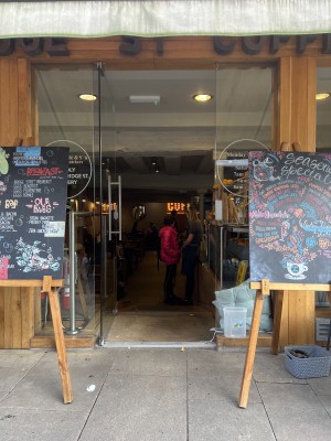Main entrance door opens inwards from right to left. Slight bump then very steep ramp downwards into cafe.