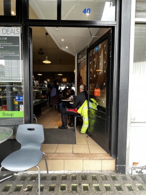 From pavement, facing straight. Glass doors with black frame. Gold handle to left. Push to open.