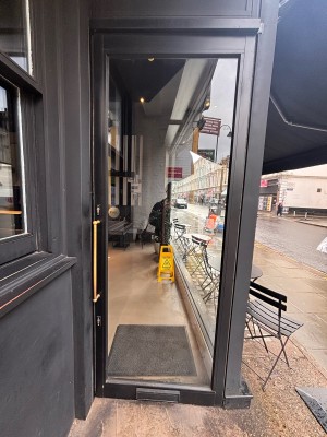 Glass door with black frame ahead. Pull metal handle at center left to open.