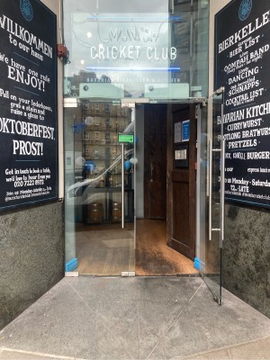 Access to venue via opening in building stone walls. Double glass doors ahead. Pull open via vertical metal handrails in center.