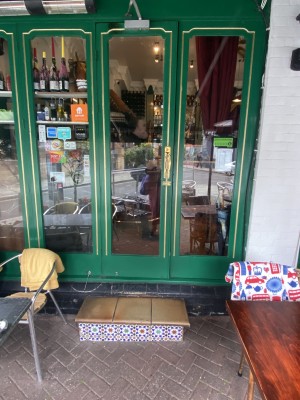 View on main entrance. Double glass pull doors with green & gold frame. Door handle on right side of left door. Two steps along front door.