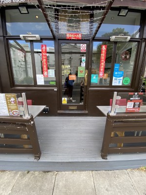 Main entrance. Go up on step, go down a pathway before you get to door. Glass push door with brown frame. Door handle on right side. One more step along door.