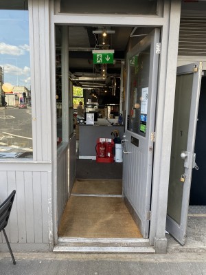 Main entrance is grey framed glass push door with door handle on left side of door. One small step along front of door.