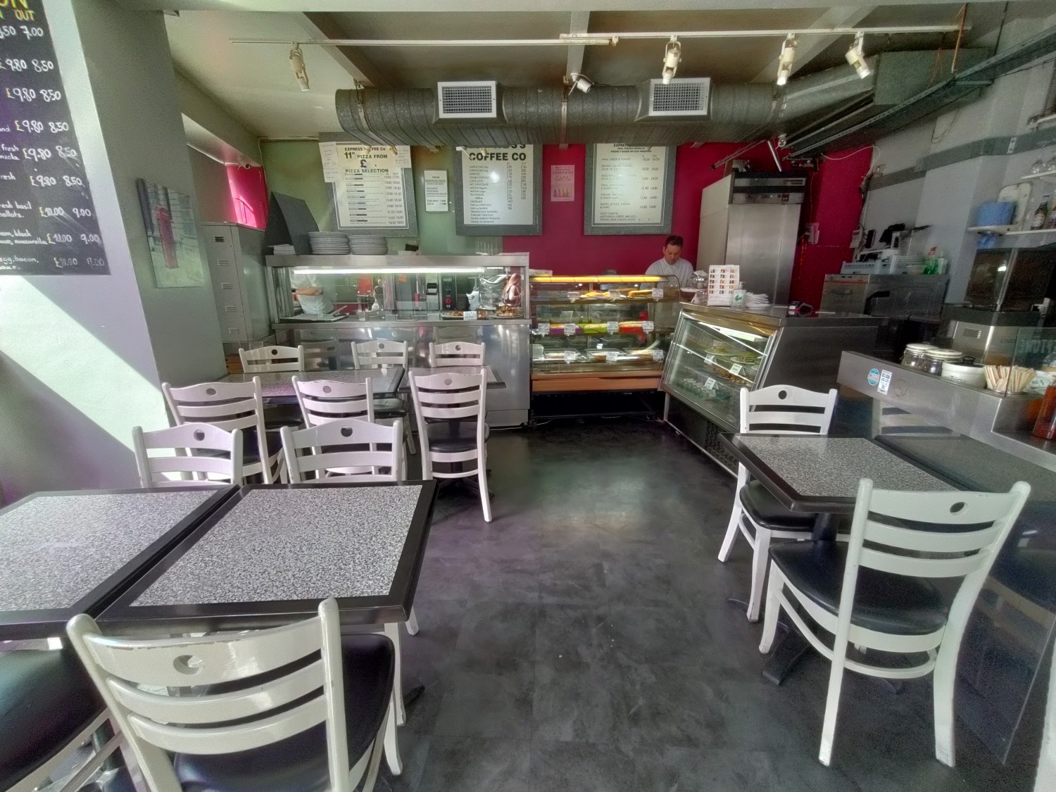From right of tables facing straight. Path ahead. Tables with chairs along left. Counter at back and back right. Small table on right.