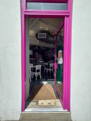 Single glass door with pink frame. Push pink metal handle on left to open.