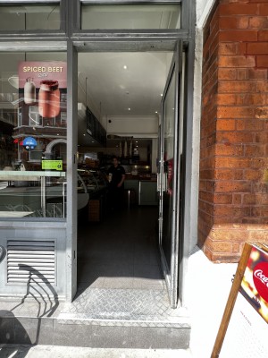 Single glass door with grey frame. Push open via metal handle left.