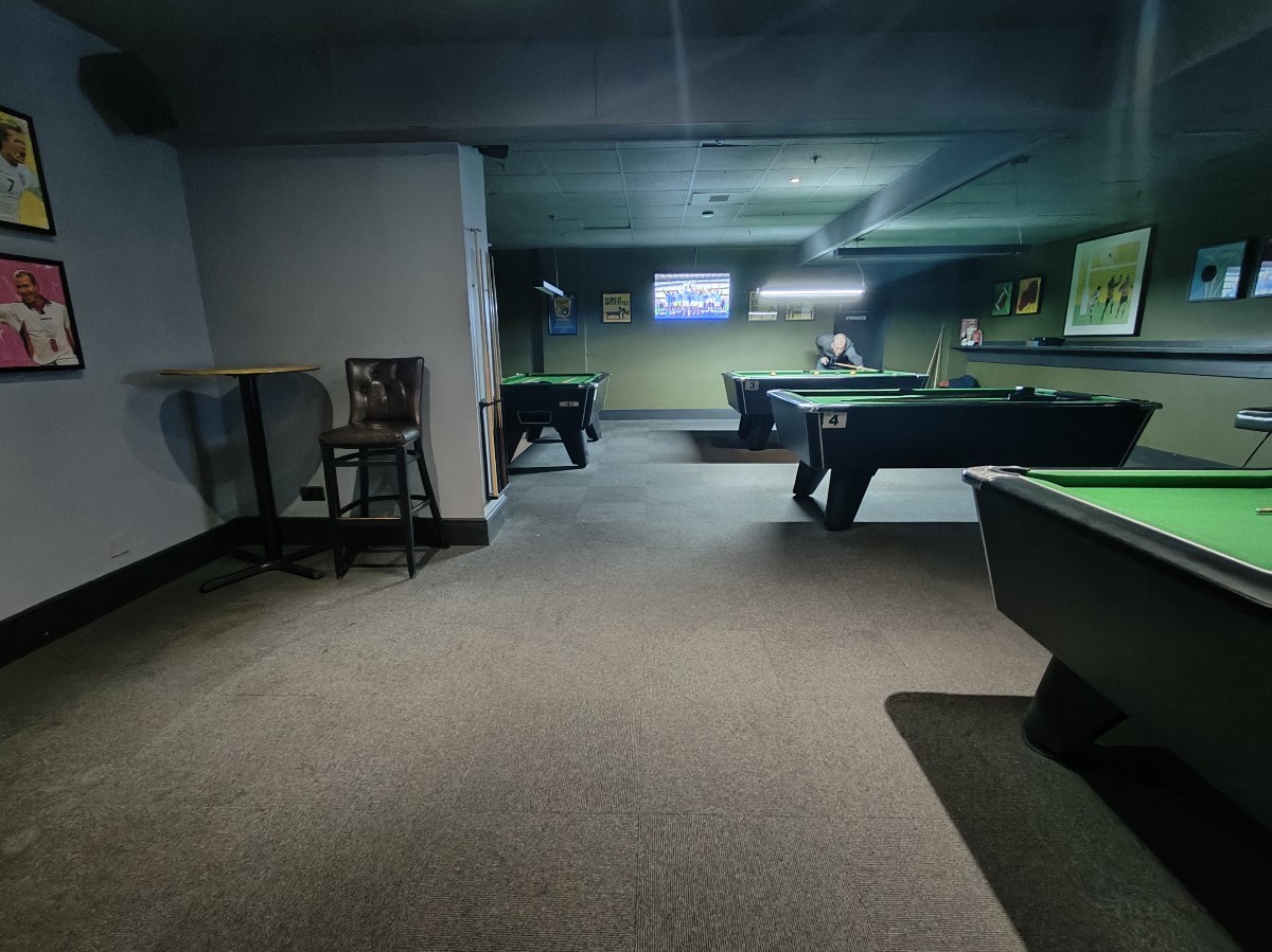 From before pool tables facing left. Stools at back left. Pool tables along right.
