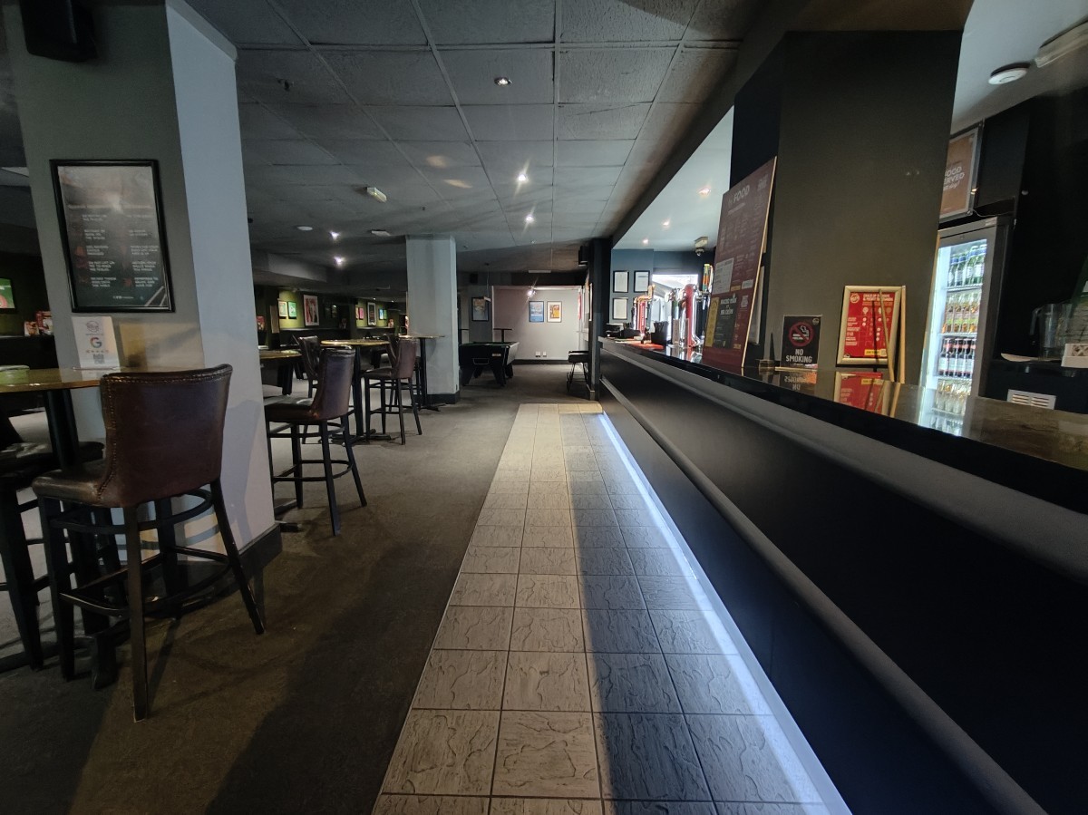 From door facing straight. Bar on right. High table and stools on left. Columns in between stools.