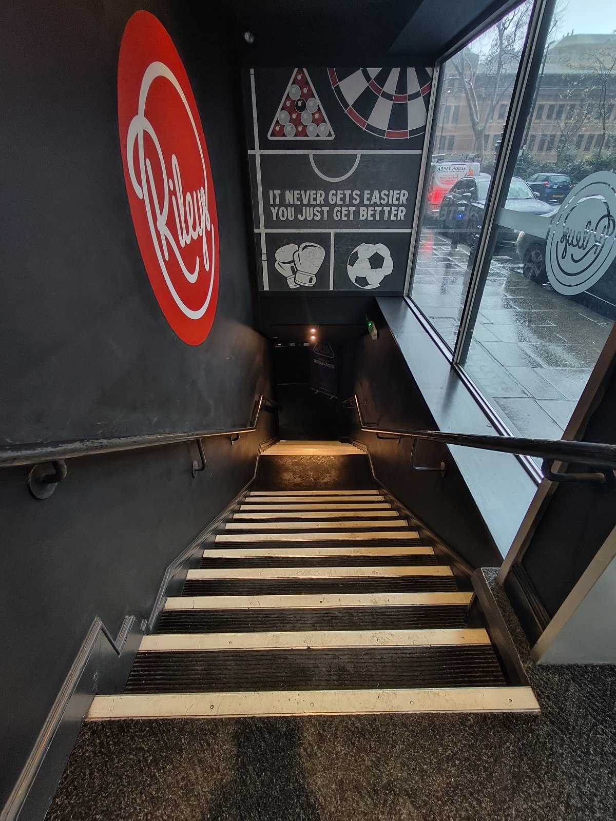From door facing left. Stairs going down ahead to landing at end. Black handrail on both sides.