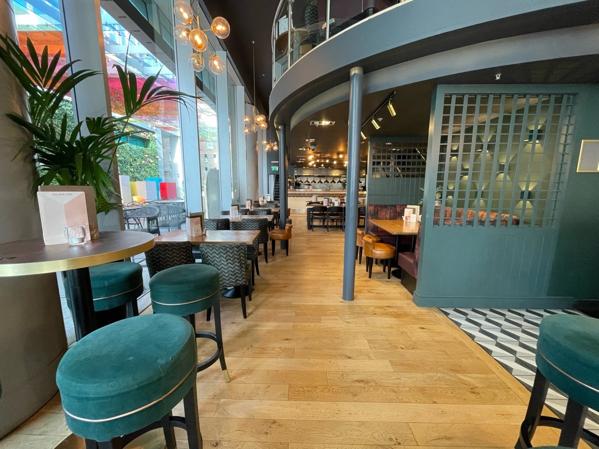 From end of high tables, facing straight. Path ahead, going straight. Pillar at back right obstructing path. Green divider at back right.