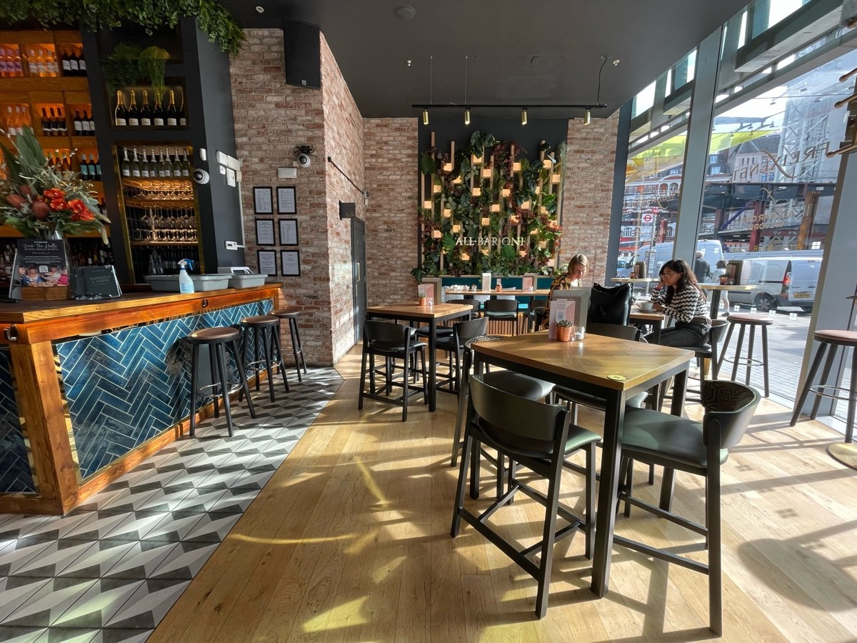 From entrance, facing straight. Bar counter along left. Path ahead, going straight. High tables spread out at back right. Glass wall on far right.