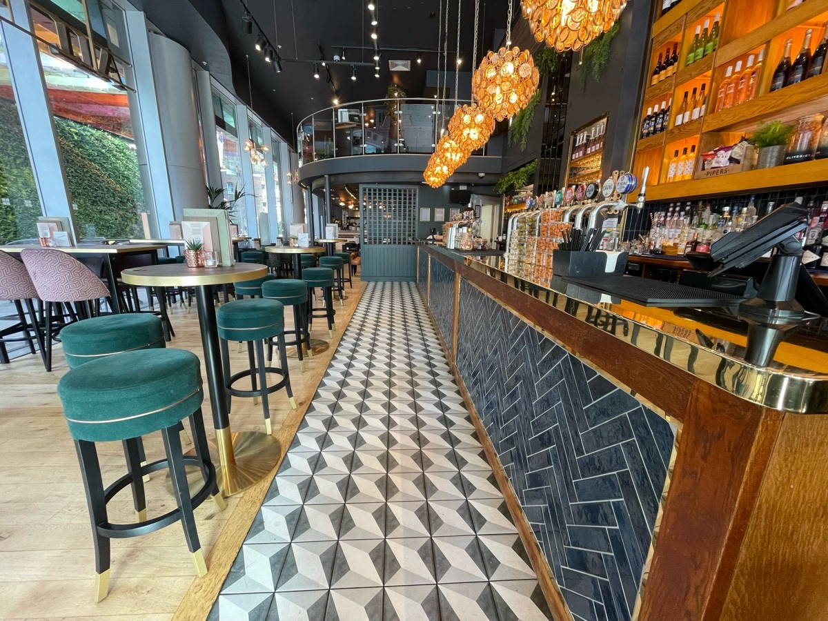 From bar, facing straight. Bar counter along right. Path ahead, going straight. High tables along left.