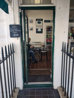 From pavement, facing straight. Path with black railings on both sides leading up to green and glass panelled door. Push black handle on right to open