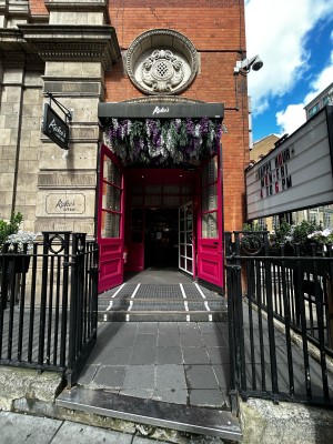 Entrance path ahead between steel fence.One step ahead to landing area.Two steps and first set of pink glass doors beyond.Handle on mid.Pull to open.