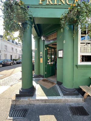 Green pillars left and right, opening in middle to entrance at back. Street path on left.